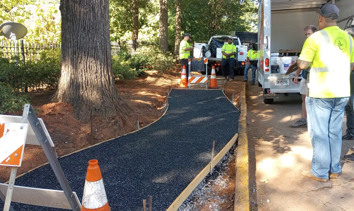 Flexus CP-200 install in Athens, Georgia: a black porous path around a large tree, with crew and cones, replacing concrete displaced by tree roots
